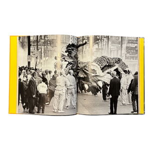 Open book showing a black and white photograph of a parade in Vancouver's Chinatown with onlookers watching lion dancers perform.